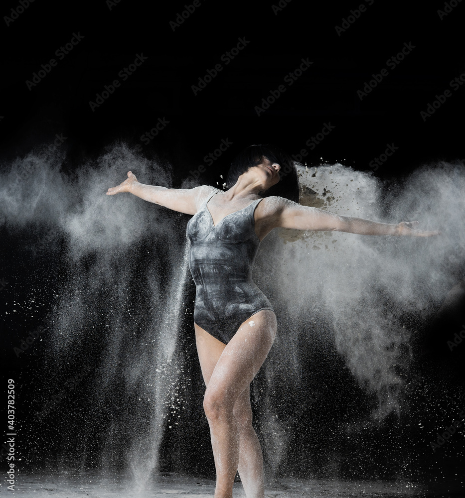 beautiful Caucasian woman throws white flour with her hands in different directions on a black background
