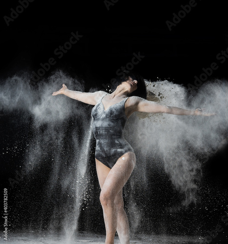 beautiful Caucasian woman throws white flour with her hands in different directions on a black background