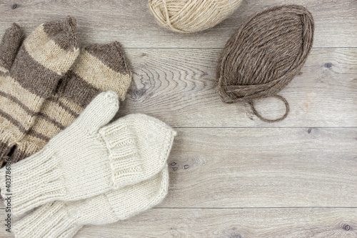 Skeins of thread and knitted mittens on a wooden background. Mittens with a flap. The concept of hobby, home production and individual entrepreneurship.