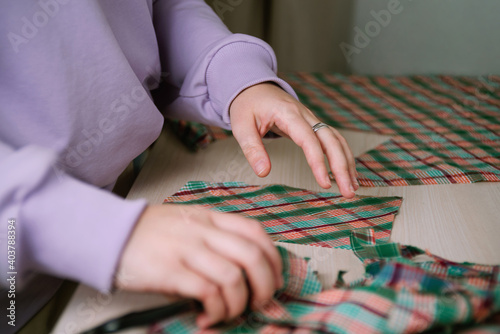 Closeup of female tailor cuting out checkered fabric with a paper pattern to make out a shirt