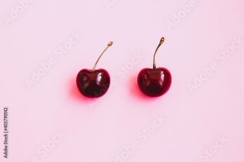 Two ripe cherries on a light pink background. Valentine's Day concept. Close-up of cherries. Summer background