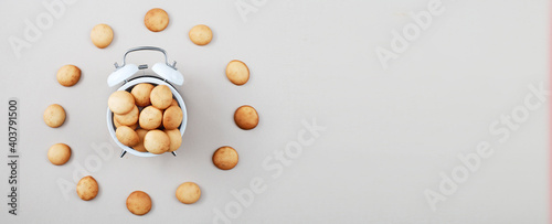 sweet cookie in form of an alarm clock, time for breakfast or dessert concept. top view. mini pancakes background