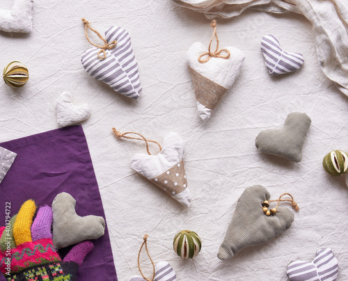 Fototapeta Naklejka Na Ścianę i Meble -  Hand made textile hearts and balls on cotton background. Hand holds soft heart. Textile stuffed toys, balls and candle in neutral colors and purple color. Flat lay, top view. Grey winter window light.
