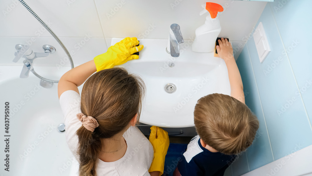 Rear view of mother with little son cleaning and washing water sink and tap in bathroom. Family doing housework and chores Rear view of mother with little son cleaning and washing water sink and tap in bathroom. Family doing housework and chores