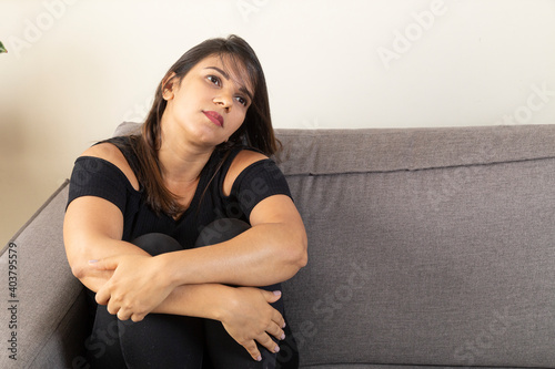 Sad woman on sofa crossing her arms.