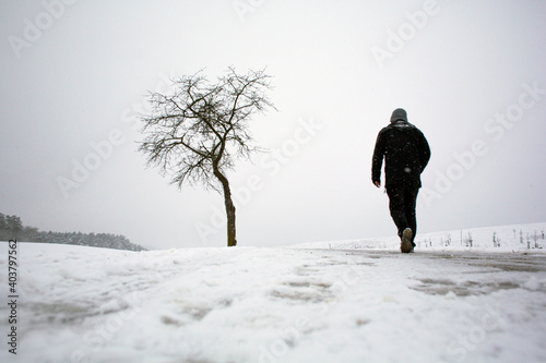 A man in black clothing seen out walking on a snowy day in Franconia, Germany as winter arrives with a cold wind and heavy snowfall.