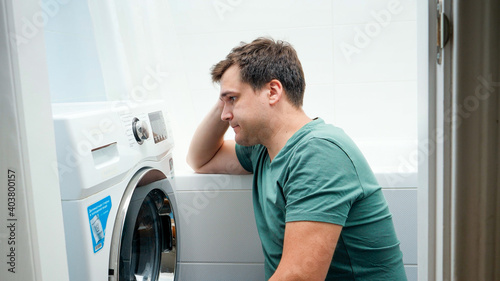 Portrait of young man struggling and getting confused while setting washing machine for laundry