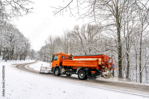 Snow ploughing truck cleans the country road leading through the forest during a snowfall