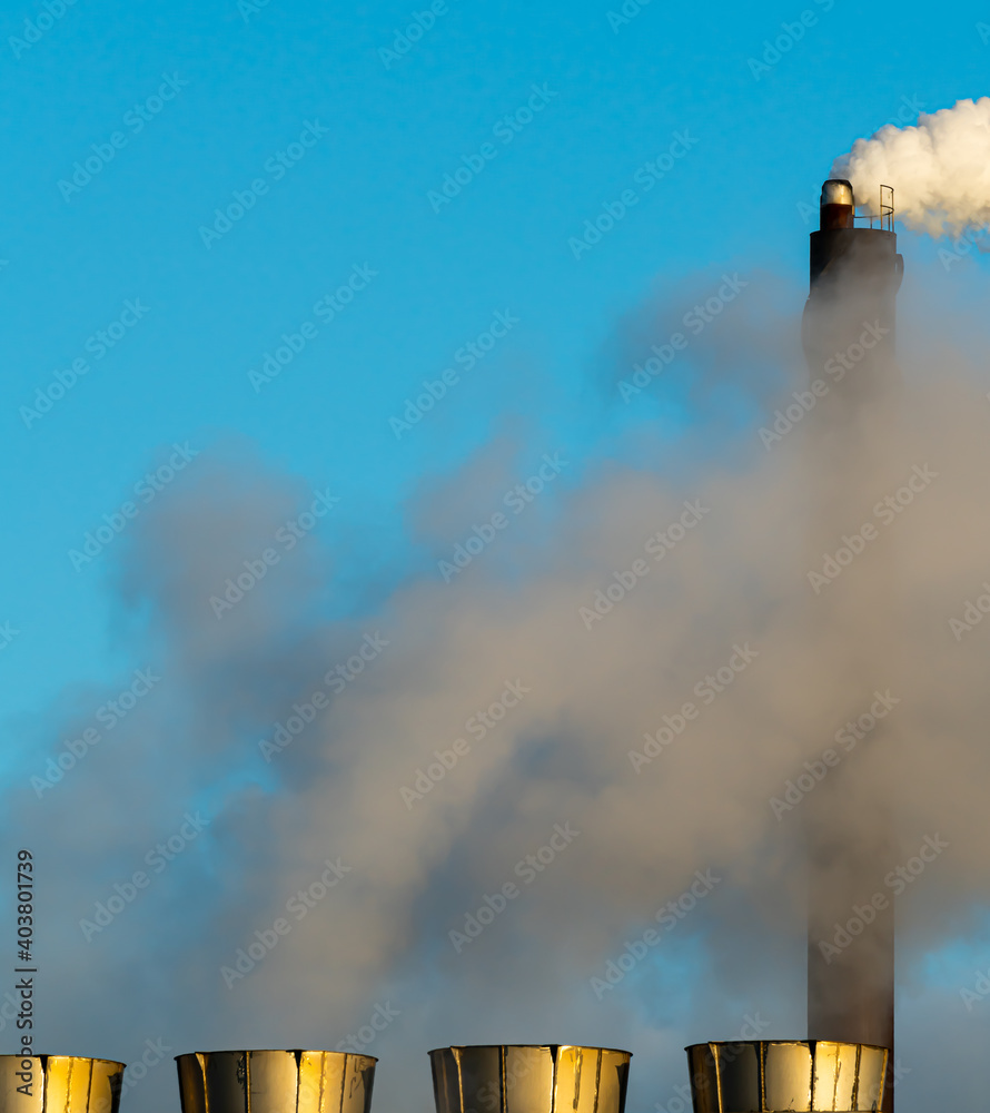 Industrial smoke stacks putting out steam and smoke on a clear blue sky.