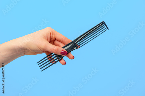 Female hand holding hair comb against blue background