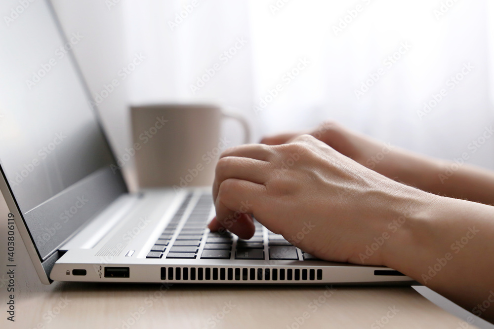 Female hands on laptop keyboard on a desk in sunlight. Woman types on the laptop keyboard sitting near the window, remote work Female hands on laptop keyboard on a desk in sunlight. Woman types on the laptop keyboard sitting near the window, remote work