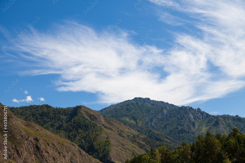 Aerial landscape with mountains, green trees, field, road and river under blue sky and clouds in summer