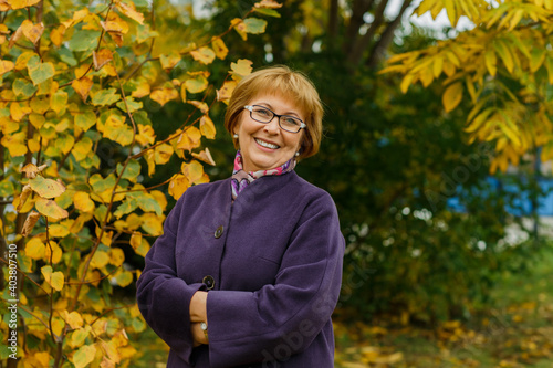 oyful portrait of a mature woman in glasses in the park in the autumn season. A smiling middle-aged lady with a positive, optimistic look. Beautiful background of yellow leaves © tatiana1987