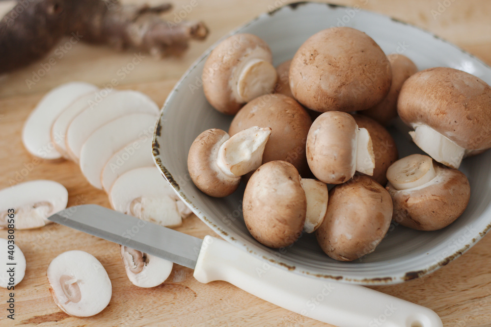 Biological brown chestnut mushrooms with sliced pieces and a knife on a wooden plate. Biological brown chestnut mushrooms with sliced pieces and a knife on a wooden plate.