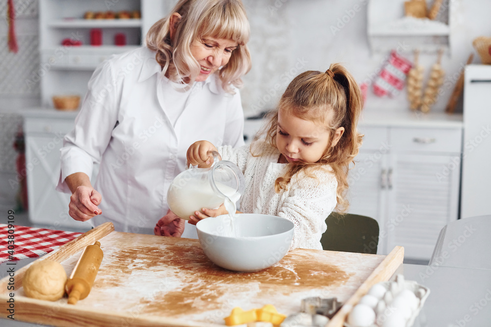 Fills with milk. Senior grandmother with her little granddaughter cooks sweets for Christmas on the kitchen