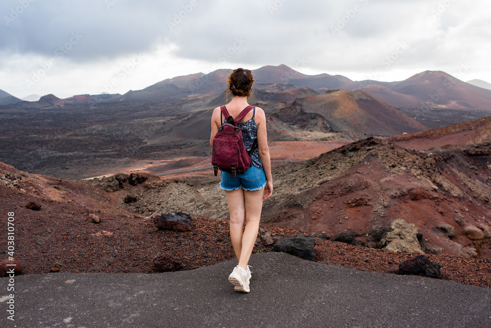 Fototapeta premium Young woman with a backpack contemplating the volcanic area Timanfaya Natural Park, in Lanzarote, travel photography