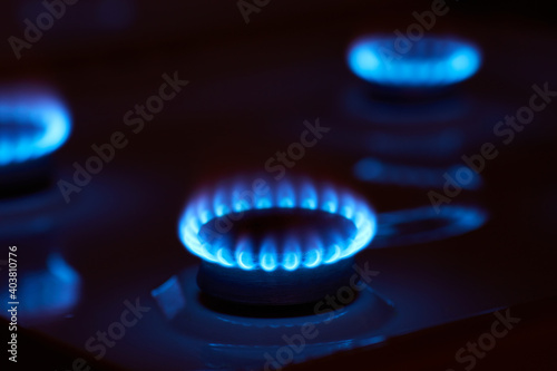 Small blue hot flame of gas burning on burner of kitchen stove at high oxygen level on dark background with lights off indoor