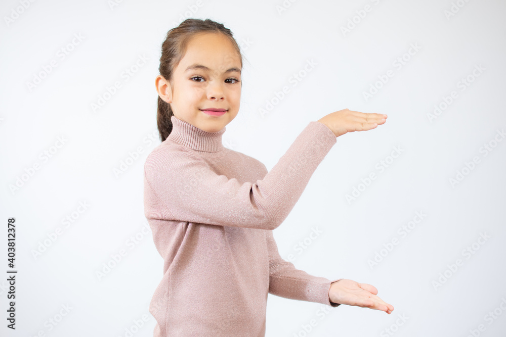 Pretty little girl in pink sweater showing product with her hands over white background. Pretty little girl in pink sweater showing product with her hands over white background.