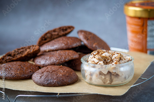 Pile of fluffy chocolate brownie cookies with a broken cookie on top served with peanut butter ice cream in a glass jar. Healthy homemade gluten free chocolate chip cookies on a cooling rack.