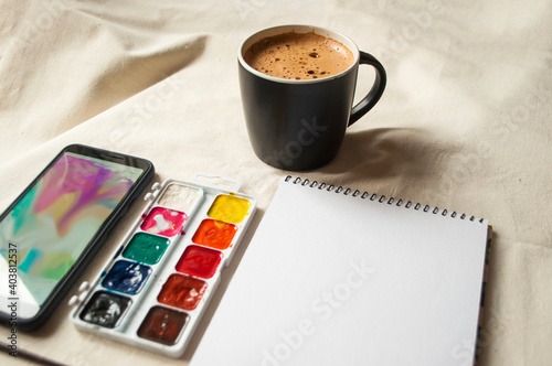 Set of watercolor paints, scetchbook, paintbrush and a cup of coffee for breakfast. photo