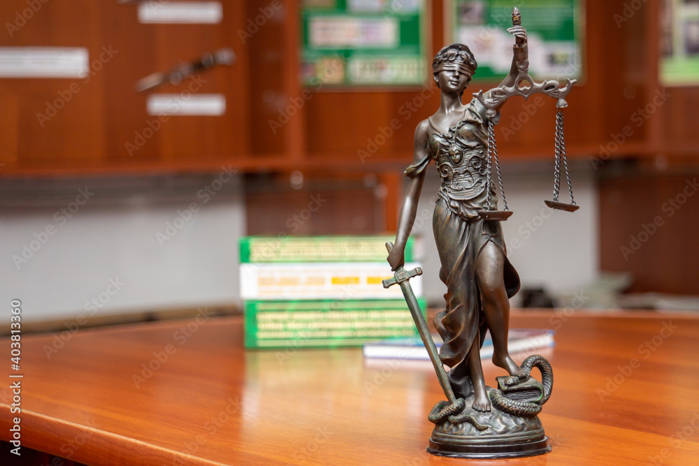 Statue of blindfolded Themis with a sword and scales in her hands, standing on a desk with books on jurisprudence in the office. Justice, human rights, advocacy, lawyering and education concept Statue of blindfolded Themis with a sword and scales in her hands, standing on a desk with books on jurisprudence in the office. Justice, human rights, advocacy, lawyering and education concept