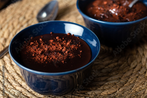 Dark chocolate mousse in a ceramic bowl on wooden table. Dark chocolate pudding with cocoa powder on top.