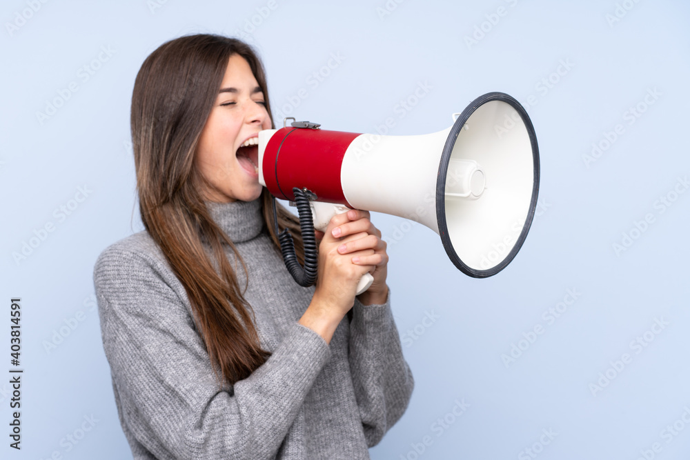 Teenager Brazilian girl over isolated blue background shouting through a megaphone Teenager Brazilian girl over isolated blue background shouting through a megaphone