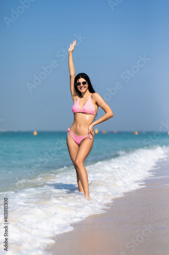 Young sexy woman in bikini walking away on the idyllic beach