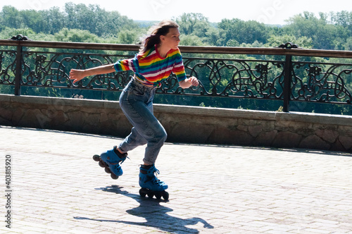 Cheerful beautiful teenage girl rollerblading in the park on a warm summer morning