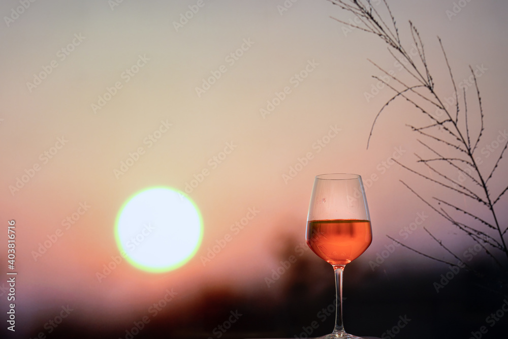 Glass of red Wine on rock with beautiful clouds of sunset or sunrise in background with blurred grass