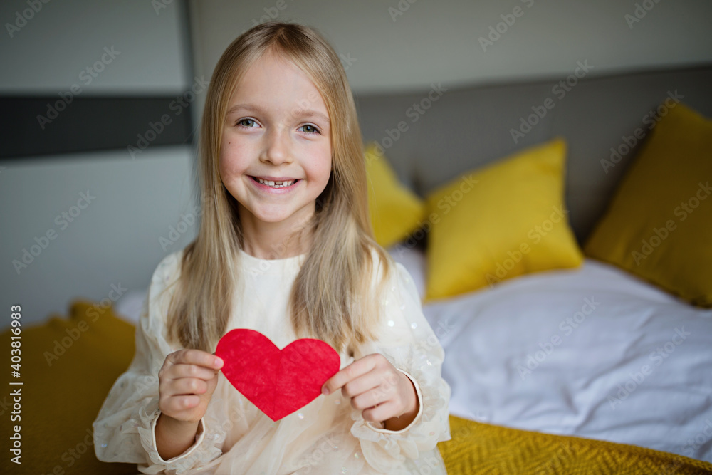 Little school kid girl holding red heart. Valentine's day during pandemic coronavirus covid-19 quarantine. Child showing heart online via video chat to boy friend Little school kid girl holding red heart. Valentine's day during pandemic coronavirus covid-19 quarantine. Child showing heart online via video chat to boy friend