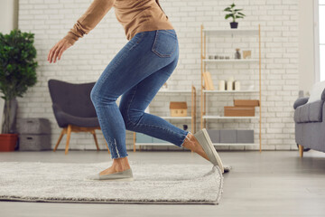 Unrecognizable female trips over rug. Clumsy faceless woman in uncomfortable shoes stumbles on rug in living-room and is about to fall on floor. Domestic accidents and getting injured at home concept