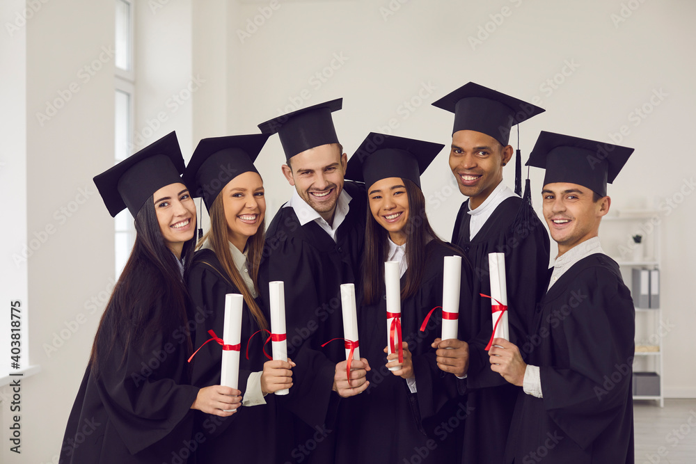 Portrait of a group of happy multiracial university graduates in academic gowns and with diplomas in their hands. Concept of successful completion of an important educational stage in life. Portrait of a group of happy multiracial university graduates in academic gowns and with diplomas in their hands. Concept of successful completion of an important educational stage in life.
