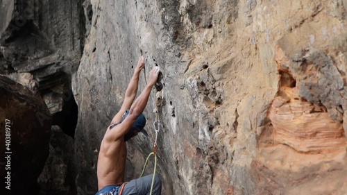 Sportive Man Training On Mountain Wall. Side view of athletic muscular man hanging on high cliff and climbing up.