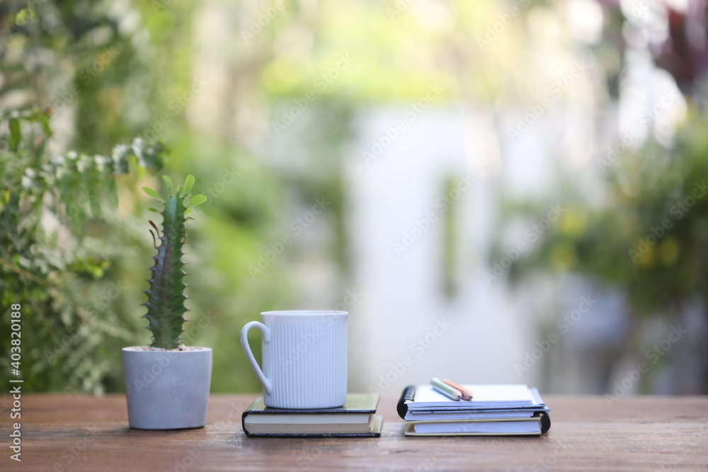 White coffee mug and cute cactus and notebooks on wooden table at outdoor