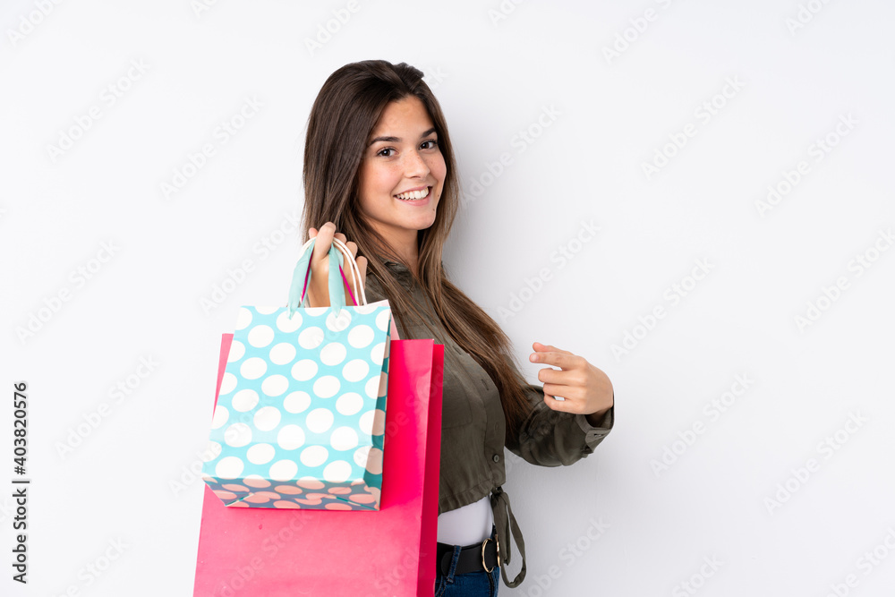 Teenager Brazilian girl with shopping bag over isolated white background and pointing it Teenager Brazilian girl with shopping bag over isolated white background and pointing it