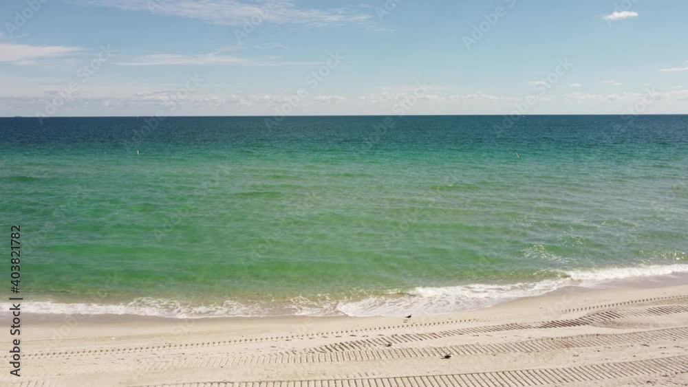 Waves crashing on the beach with tire tread tracks by the shore