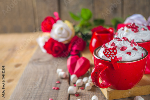 Valentine hot chocolate or coffee, Two red cups with hot chocolate or latte drink, with whipped cream ans sugar heart sprinkles, with roses bouquet ad gift box