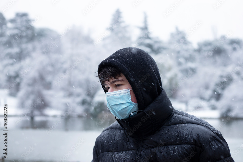 boy outside snowing with surgical mask and black coat boy outside snowing with surgical mask and black coat