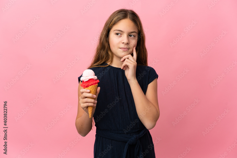 Child with a cornet ice cream over isolated pink background thinking an idea while looking up