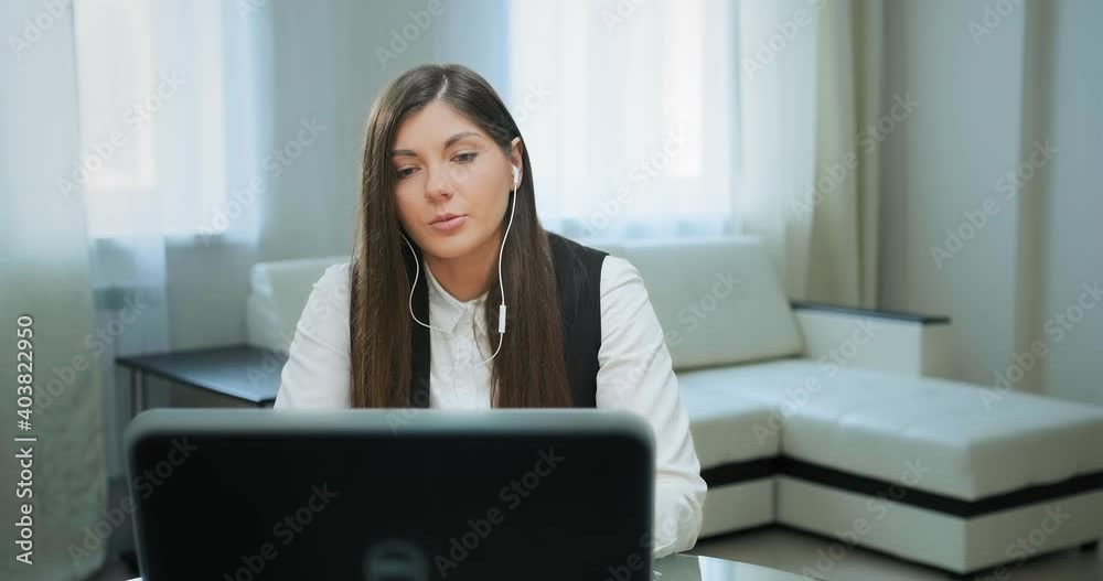 Call centre female worker with white headphones talks to customer sitting at black laptop against white sofa at home quarantine Call centre female worker with white headphones talks to customer sitting at black laptop against white sofa at home quarantine
