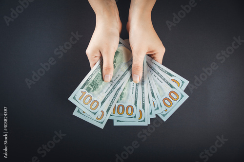 Fan of dollars in a female hand on a black background close up