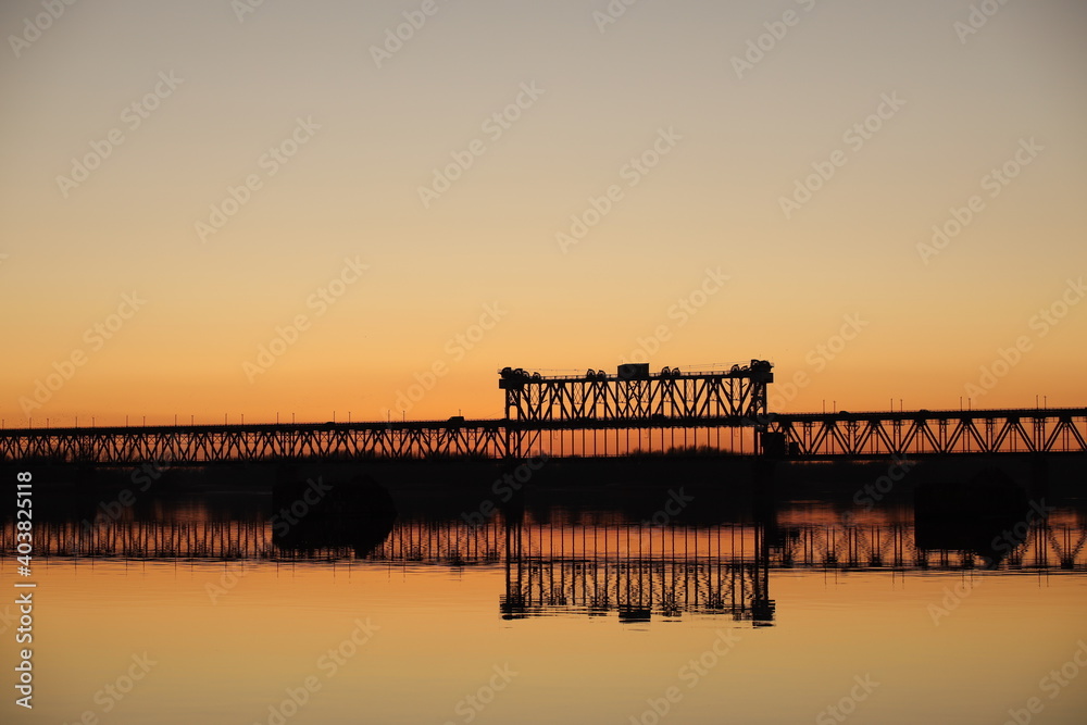 The bridge over the Dnieper against the background of an orange sunset. Kryukovsky road-railway bridge in Kremenchug, Ukraine. Industrial silhouette against the backdrop of a natural phenomenon