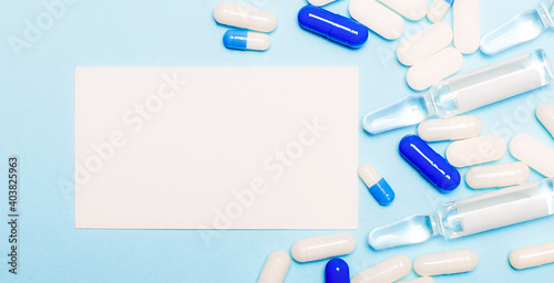 Pills, ampoules and a blank white card for text on a light blue background. Medical concept