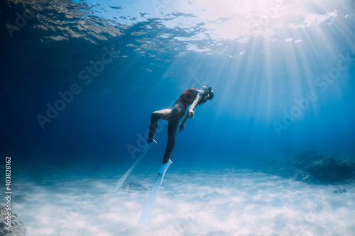 Attractive woman freediver with white fins posing underwater in sea.