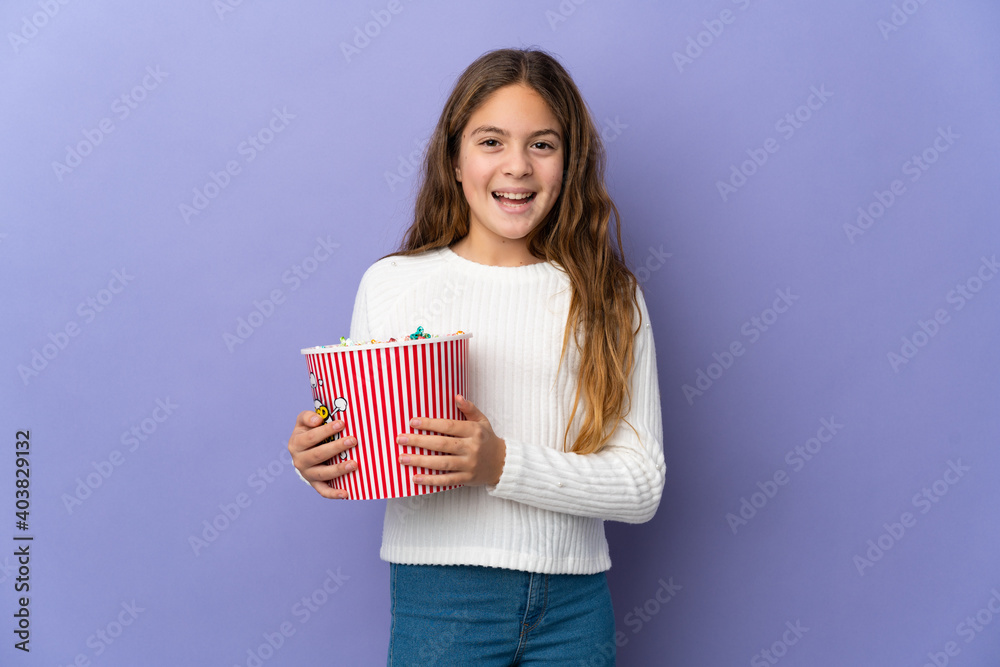 Child over isolated purple background holding a big bucket of popcorns Child over isolated purple background holding a big bucket of popcorns
