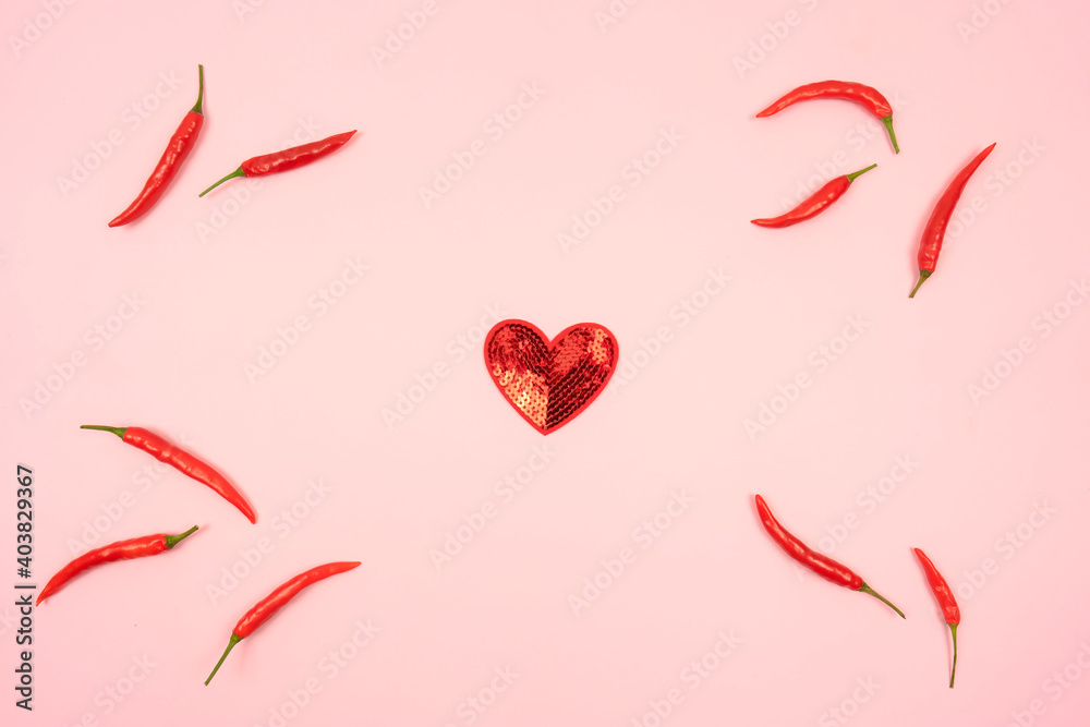 A red heart and red hot chili peppers around it lie on a pink background A red heart and red hot chili peppers around it lie on a pink background