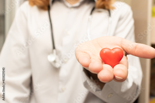 Woman doctor with stethoscope holding heart in palm