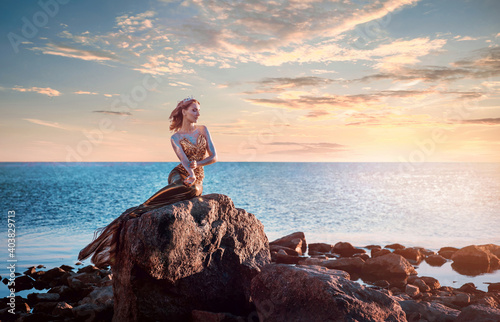 Sadness mermaid, nixie, water nymph sitting on stone. Sea, sunset view photo