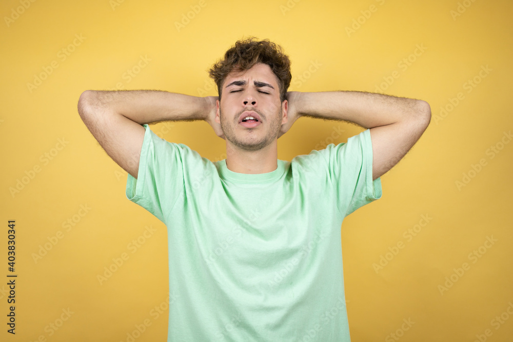 Handsome man wearing a green casual t-shirt over yellow background relaxing and stretching, arms and hands behind head and neck smiling happy Handsome man wearing a green casual t-shirt over yellow background relaxing and stretching, arms and hands behind head and neck smiling happy